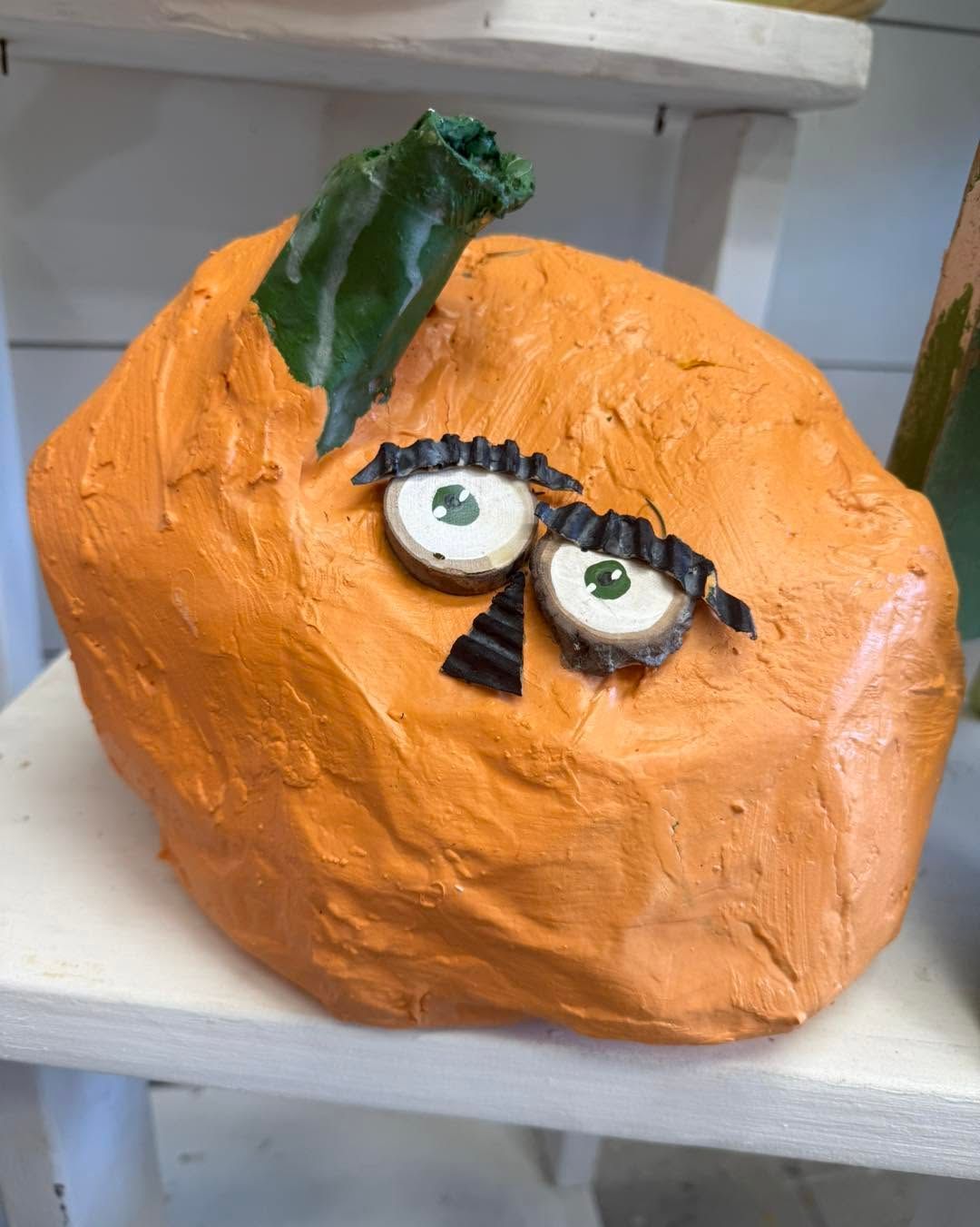 Orange pumpkin craft with googly eyes and a green leaf on a white shelf