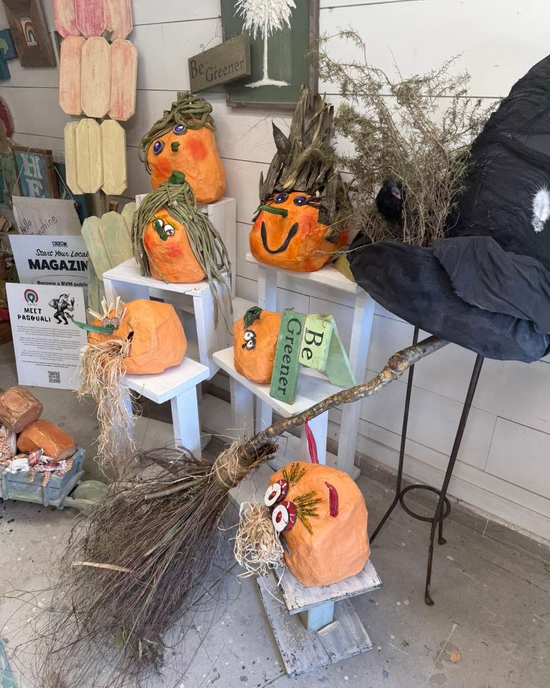Painted pumpkin scarecrows on a porch display, with straw, a broom, and a small sign.
