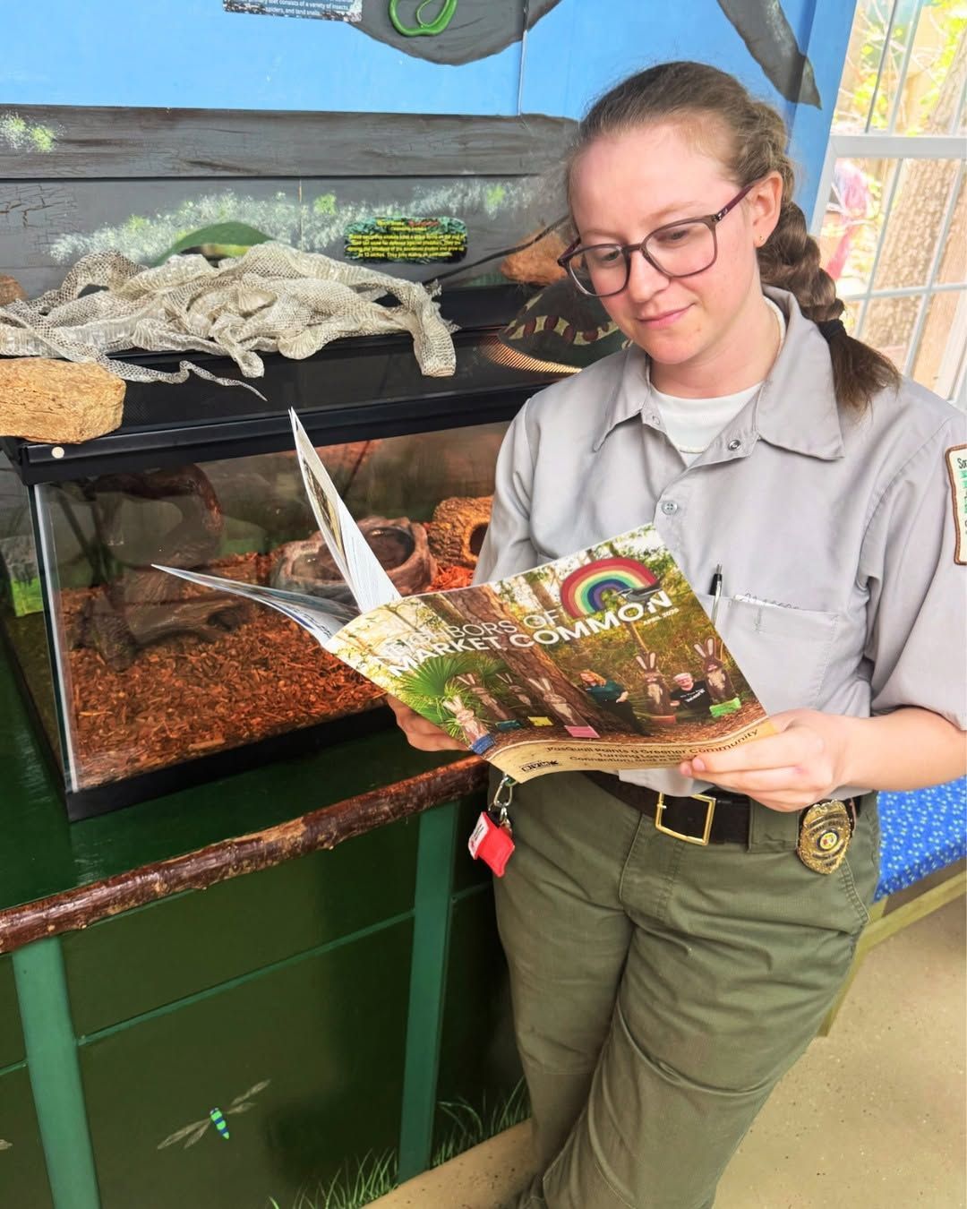 Person reading a brochure beside a large reptile enclosure with a snake inside