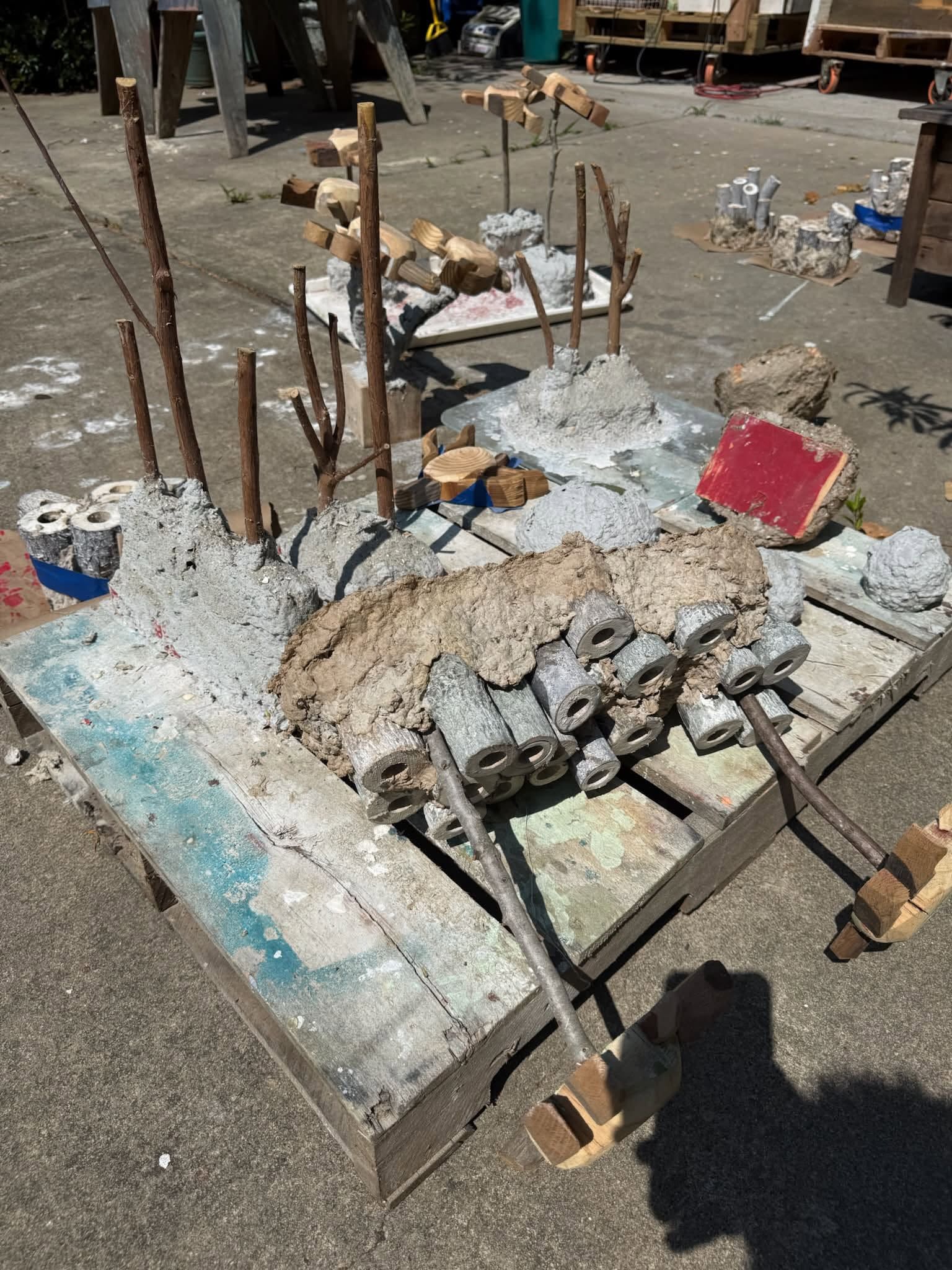 Large concrete sculpture with protruding metal rods on a wooden pallet outdoors, with debris nearby
