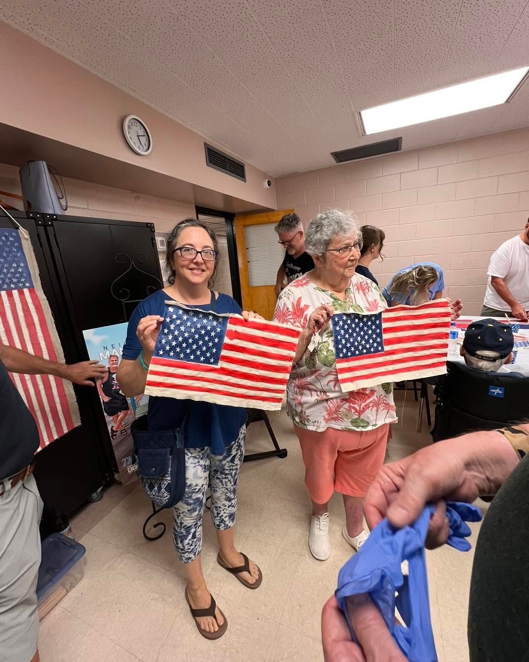 People holding small American flags in a room, smiling at an indoor gathering.