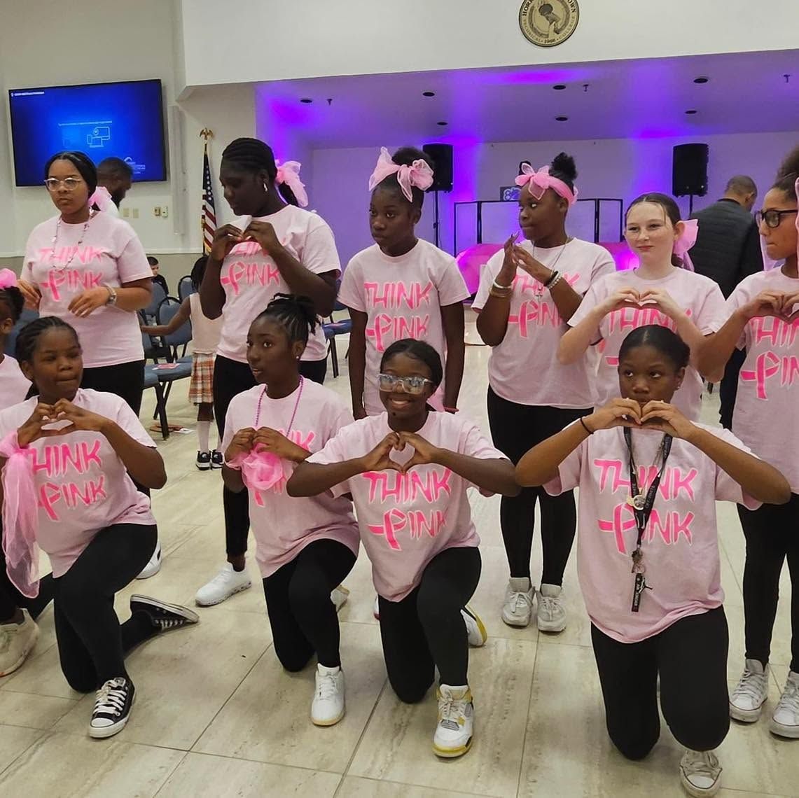 Dance group posing in pink shirts and black shorts in a bright indoor hall