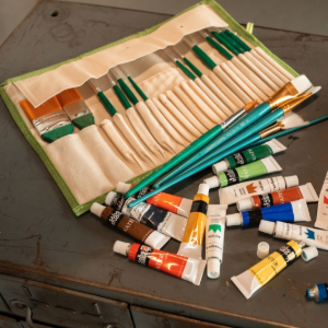 Paintbrush set in a beige roll-up case with tubes of paint scattered beside it on a table.