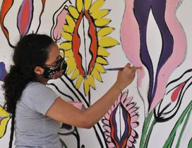 Person painting a colorful floral mural on a wall while wearing a mask