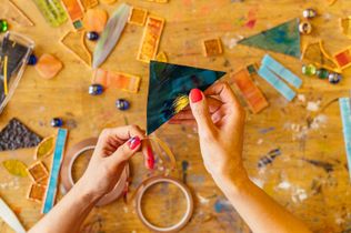 Hands crafting a paper star on a paint-splattered worktable with art supplies and scissors