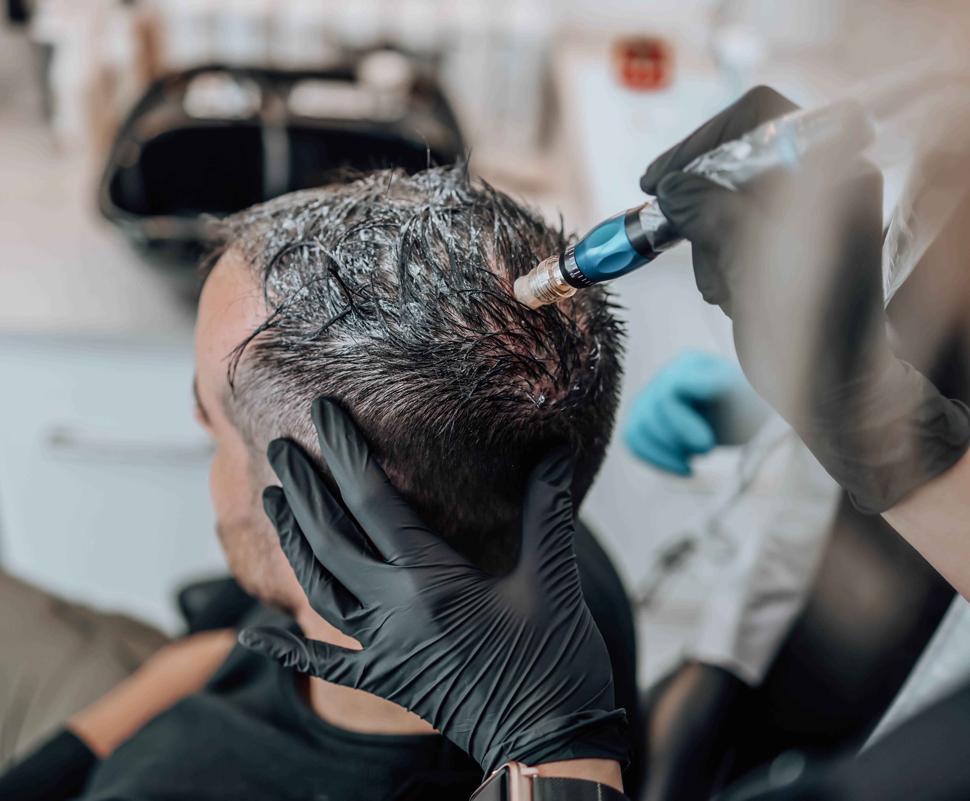 Person receiving scalp treatment; medical device used, gloved hands, salon setting.