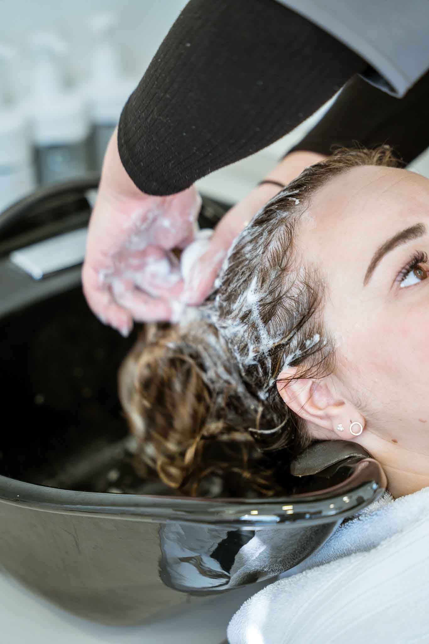 A person receives a professional hair wash in a salon, with soapy lather being applied to their hair.