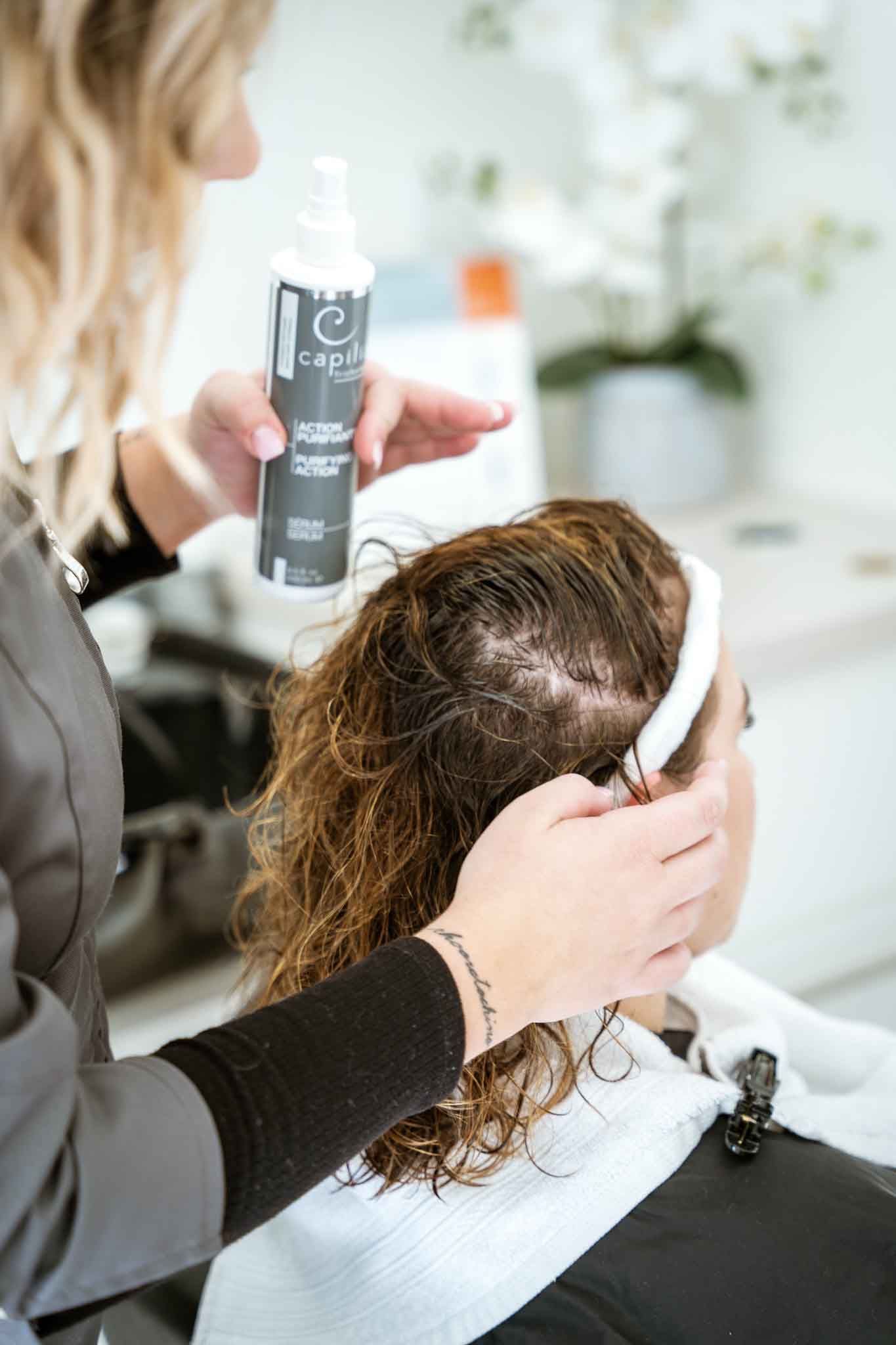 A professional applies a spray bottle of hair product to a client's damp, curly hair in a salon setting.