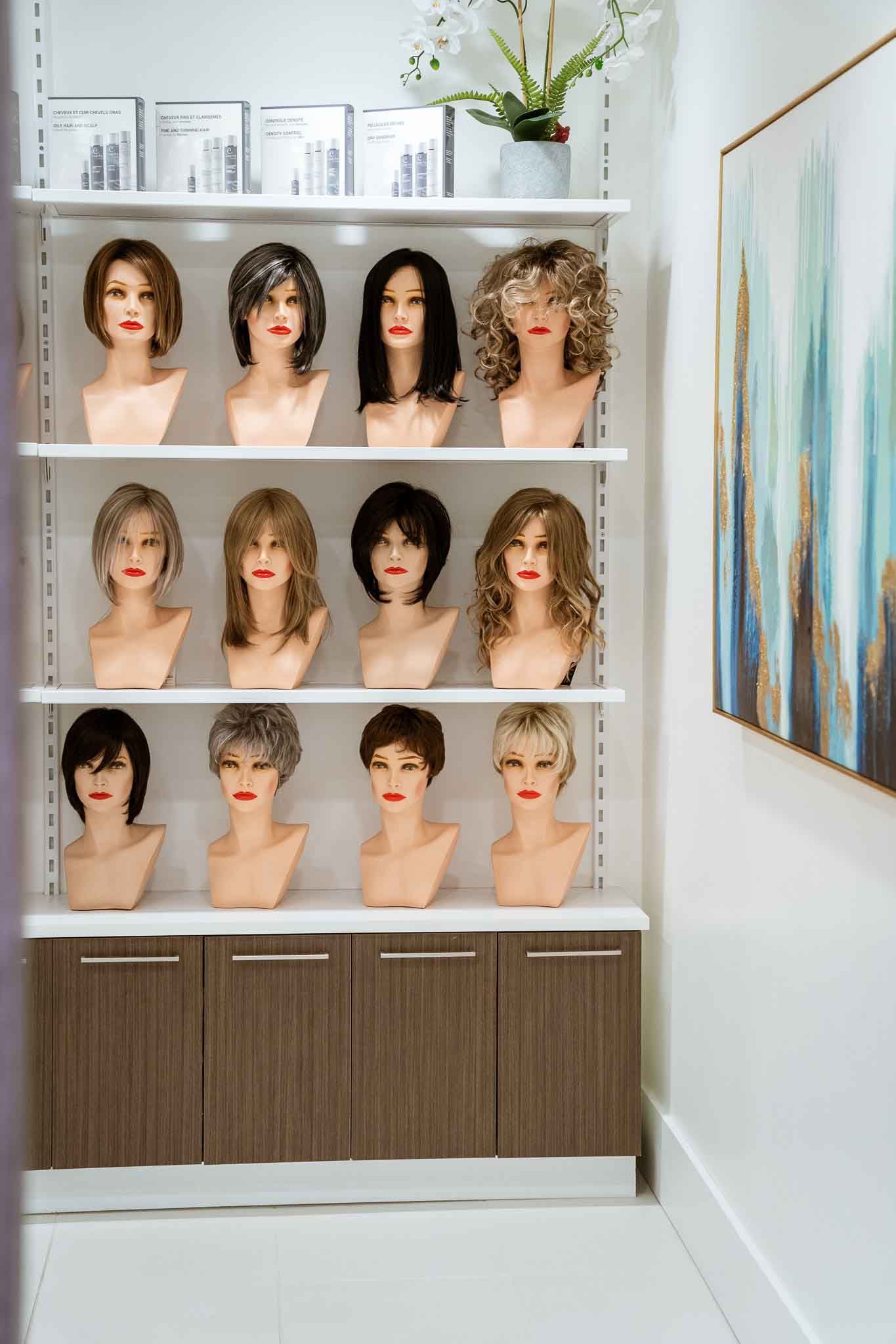Des étagères remplies de perruques de styles variés sur des têtes de mannequins, avec une grande peinture abstraite bleue et or sur le mur de droite.