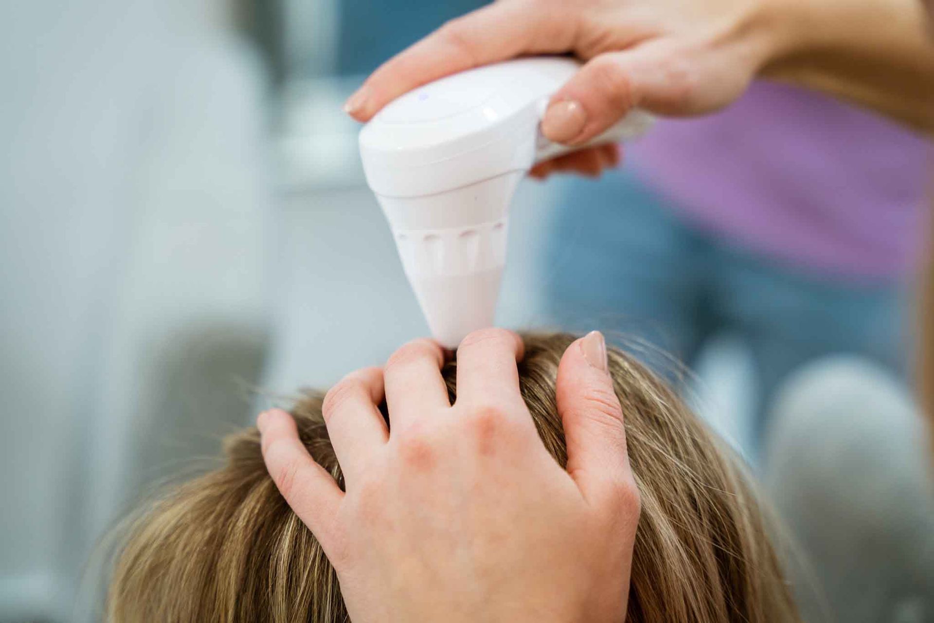 A handheld medical device is used to examine a person's scalp and hair during a clinical or professional consultation.