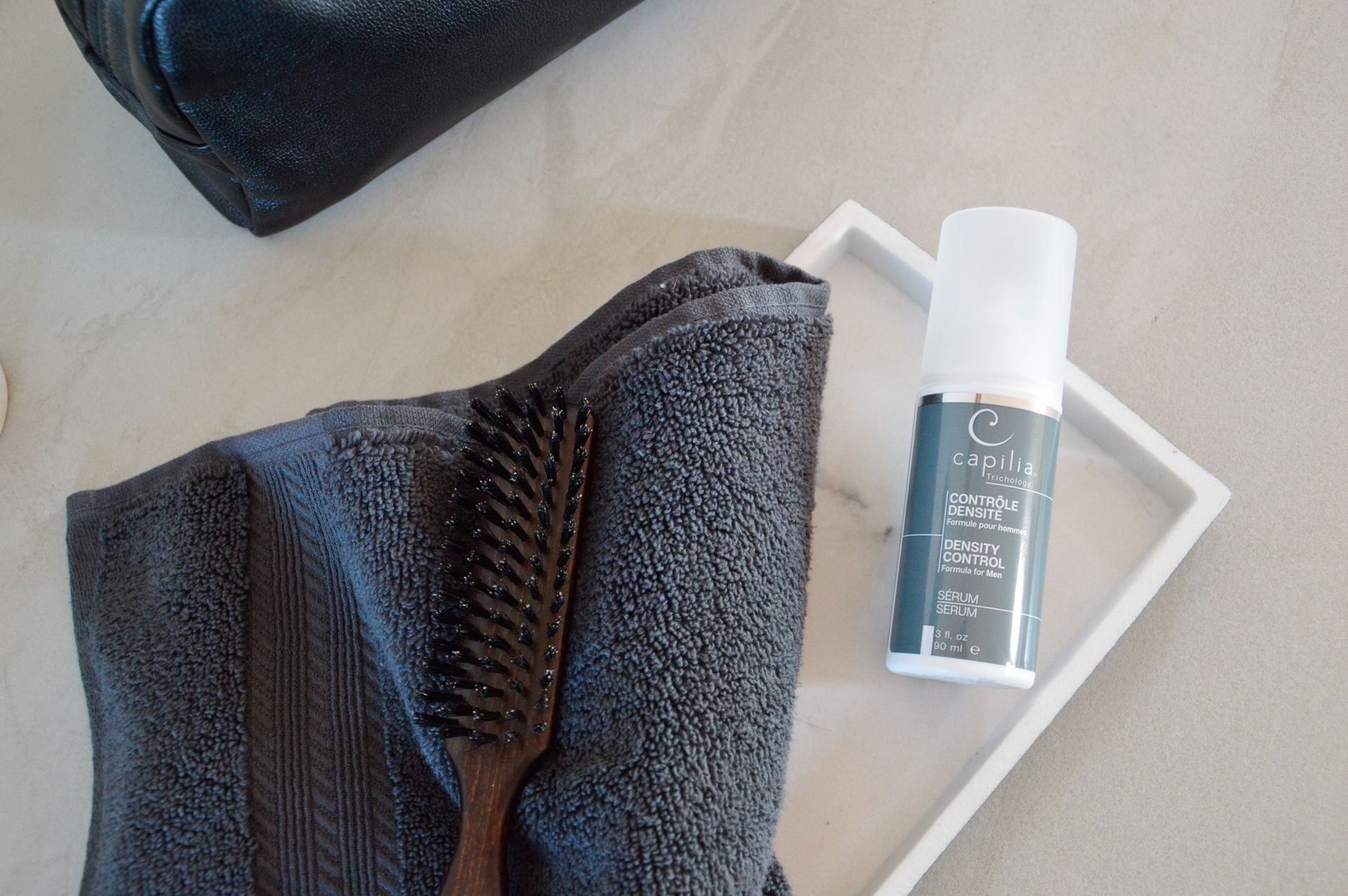 A makeup bag, towel with brush, and skincare product on a tray.