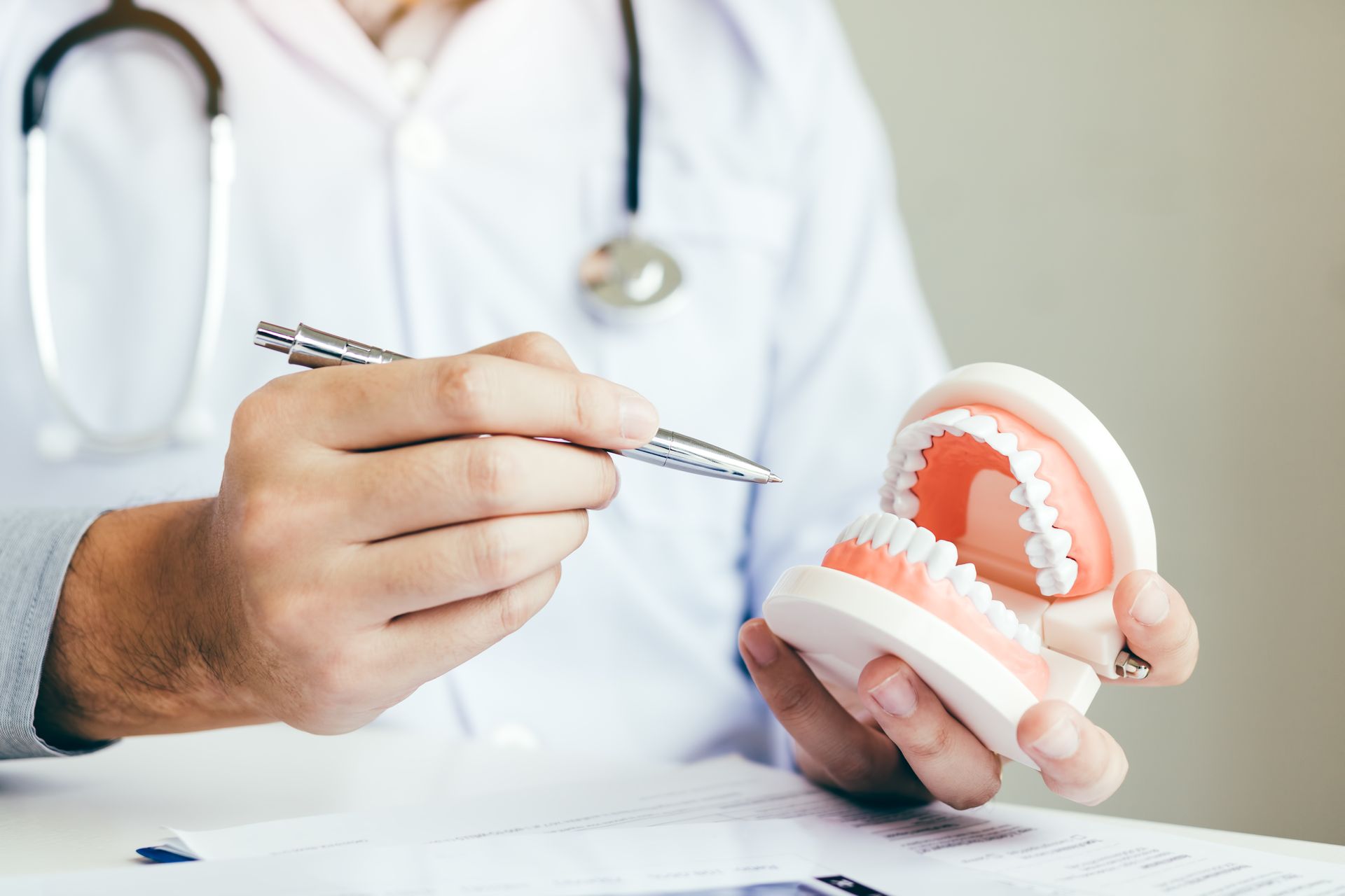Dentist pointing at a model of teeth with a dental tool in a clinic setting