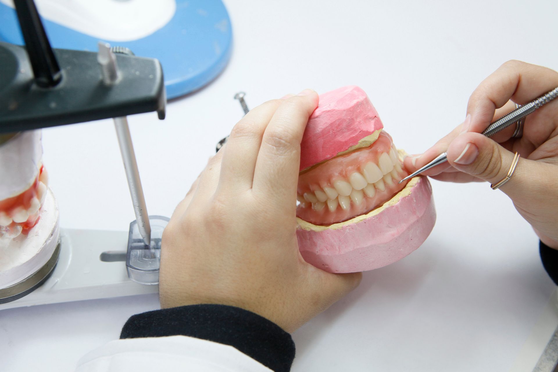 Dentist cleaning a pink model of teeth with dental tools at a clinic chair