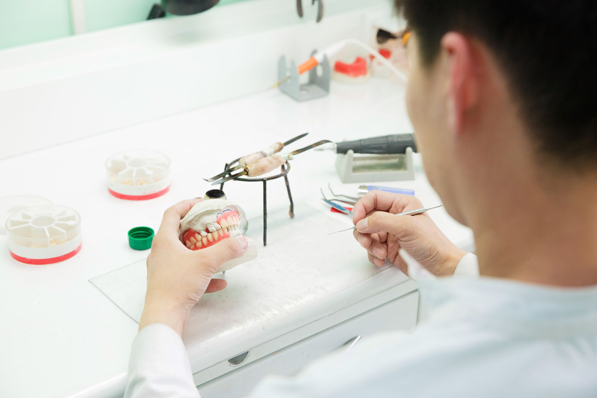 Dentist examining dental mold at a workbench with tools and plastic models