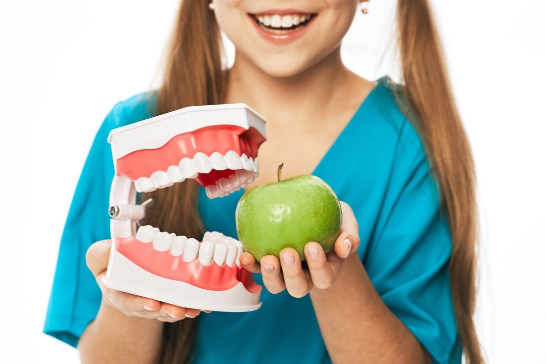 Woman holding a green apple beside a dental model with open mouth and teeth