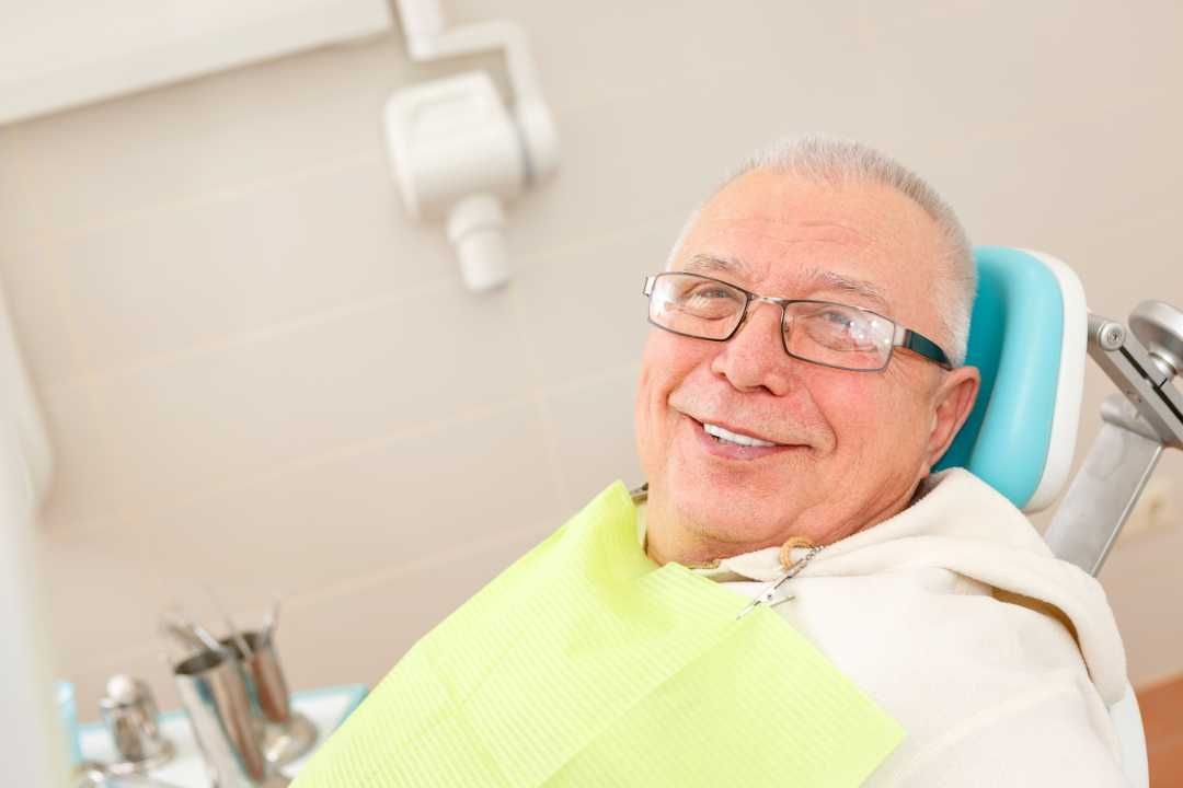 Smiling patient in a dental chair wearing a bib and glasses