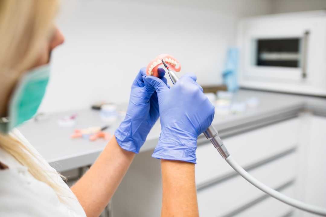 Gloved hands holding a dental tool near a patient chair in a bright clinic lab