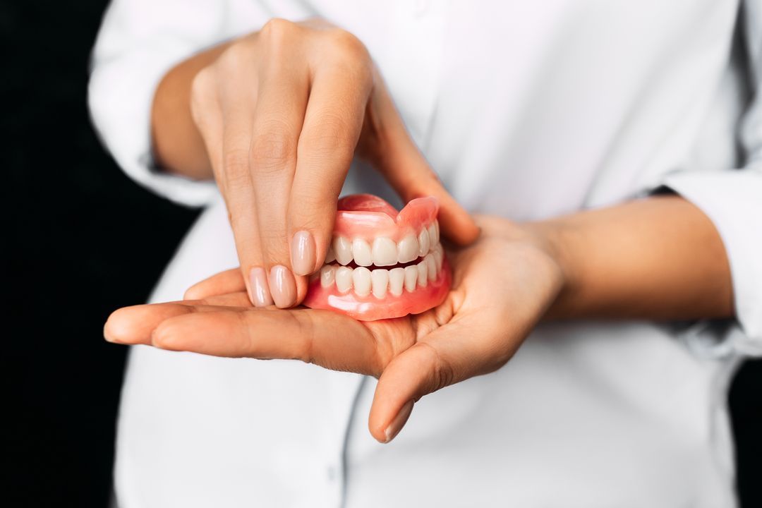 Hands holding a dental model with pink gums and white teeth in a clinic setting