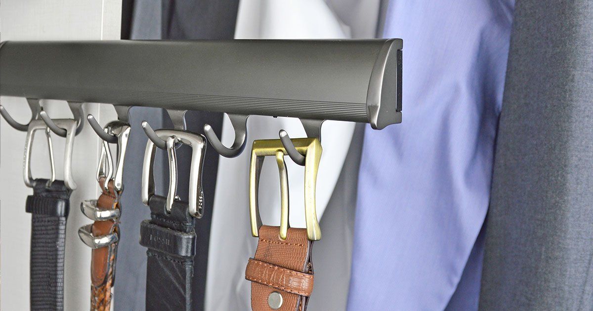 A bunch of belts are hanging on a rack in a closet