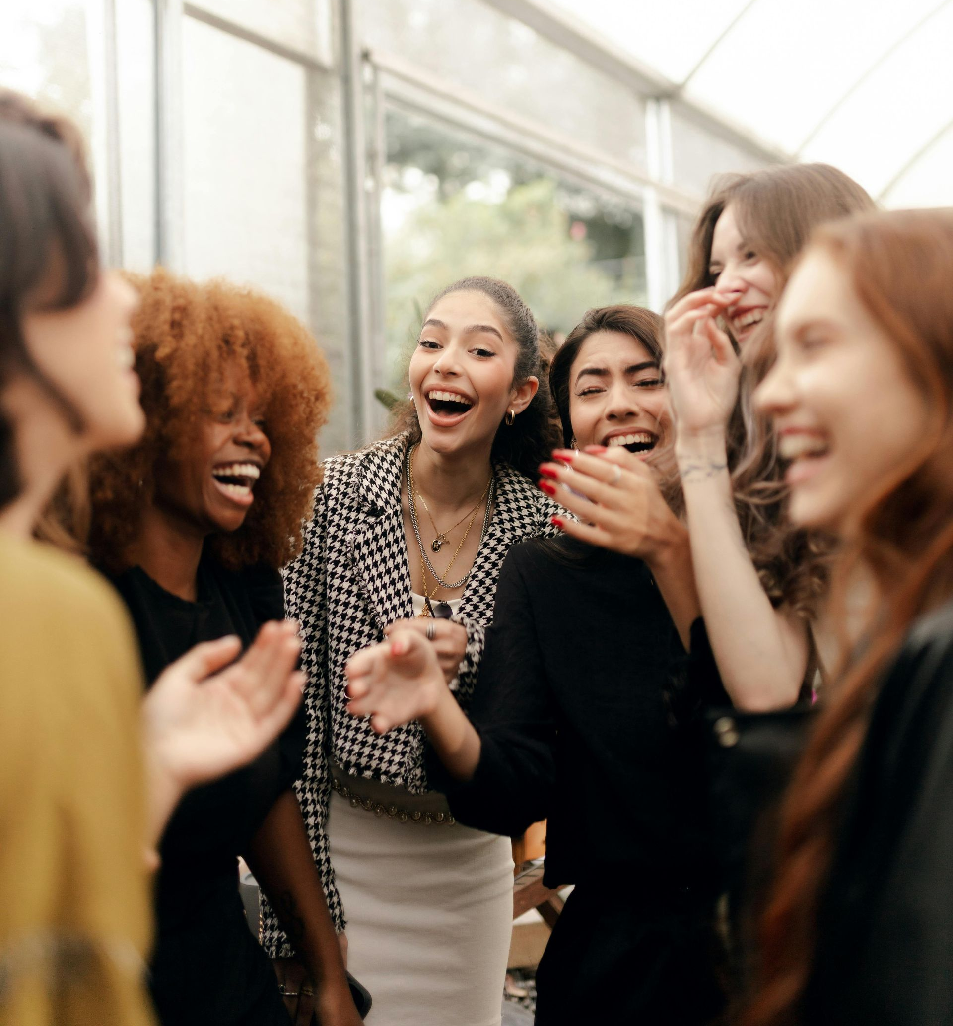 A group of people laughing together inside a bright, sunlit greenhouse.
