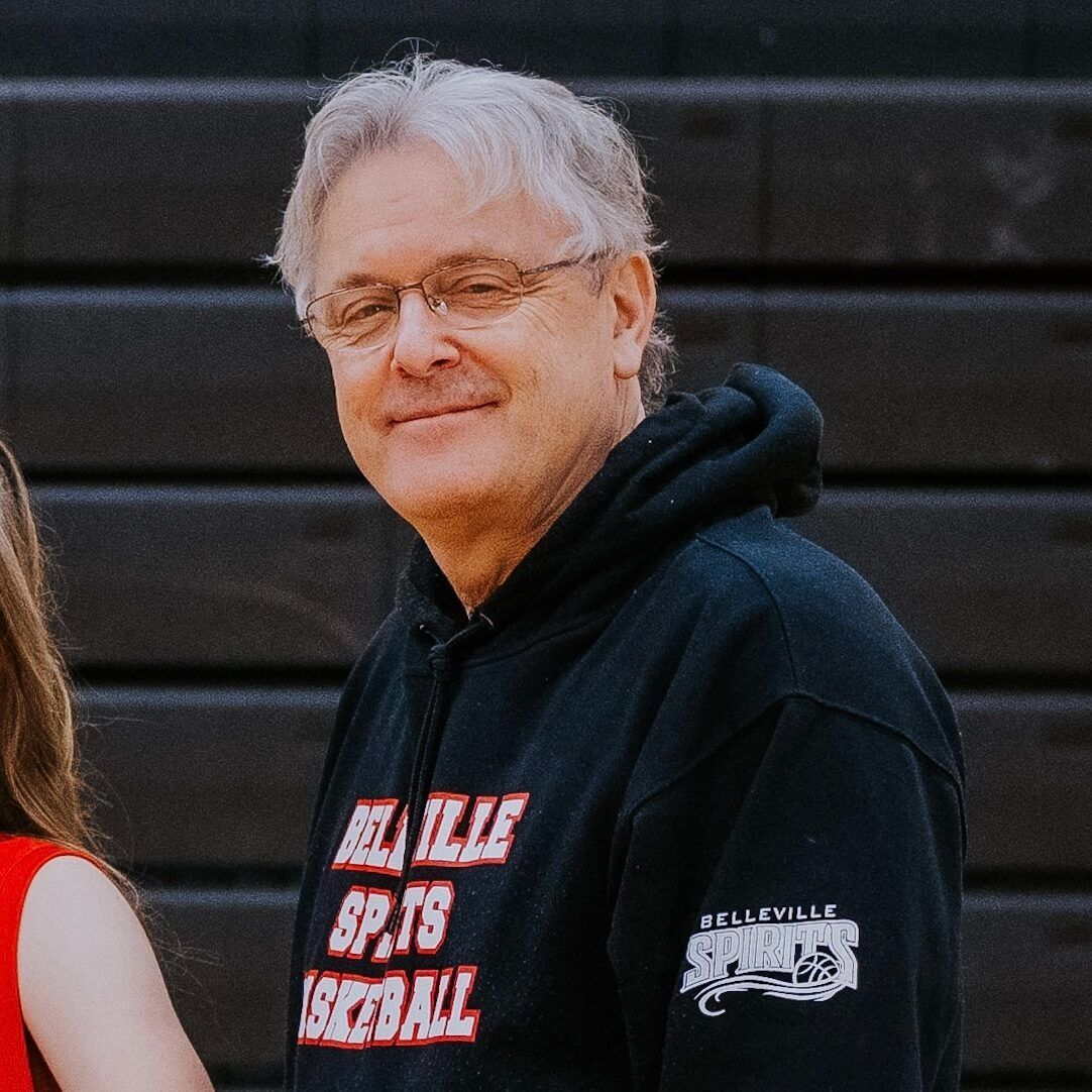 Smiling man in a black hoodie standing outdoors against a dark wall