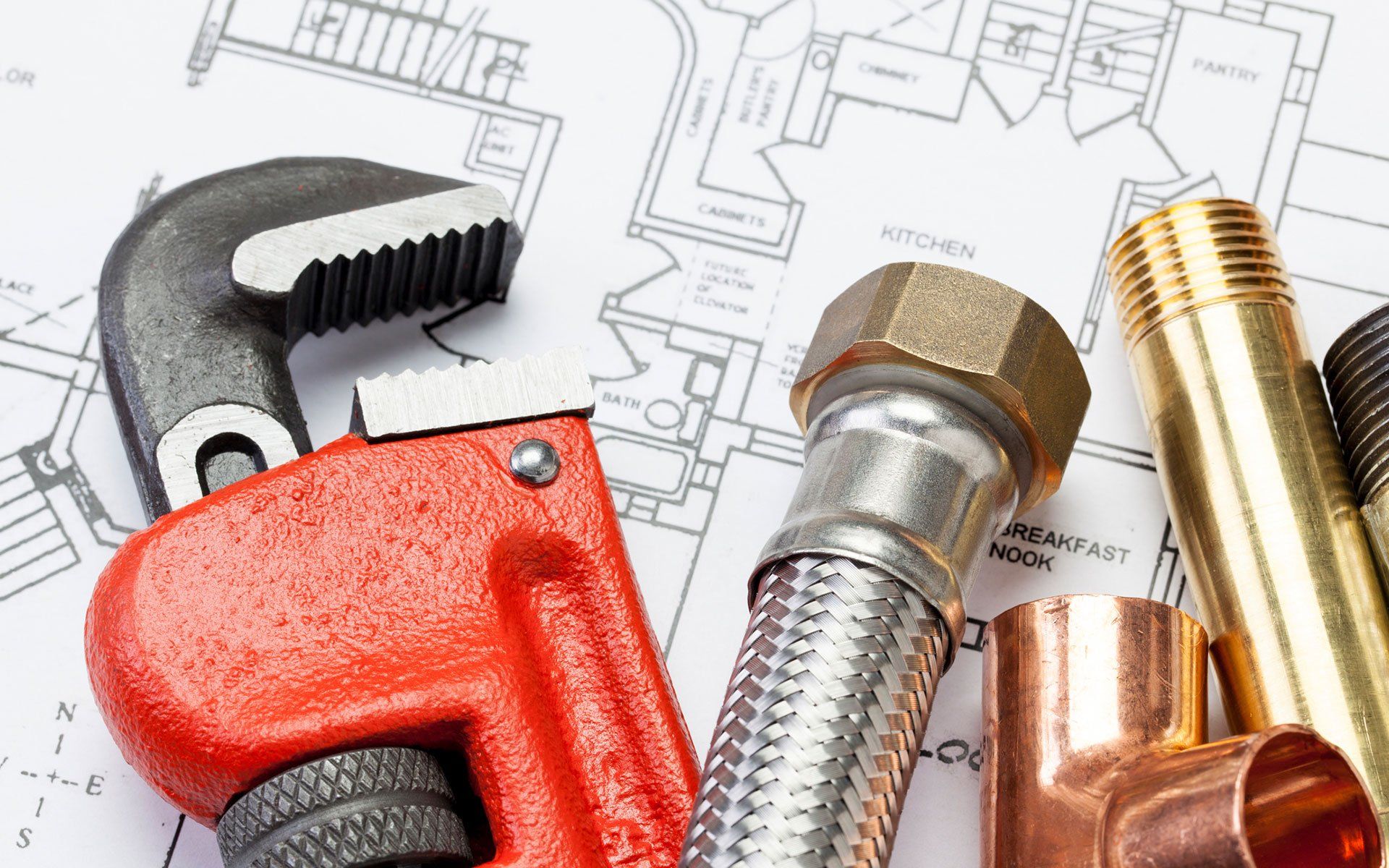 Plumbing tools, including a wrench, pipe fittings, and flexible hose, on top of a blueprint.