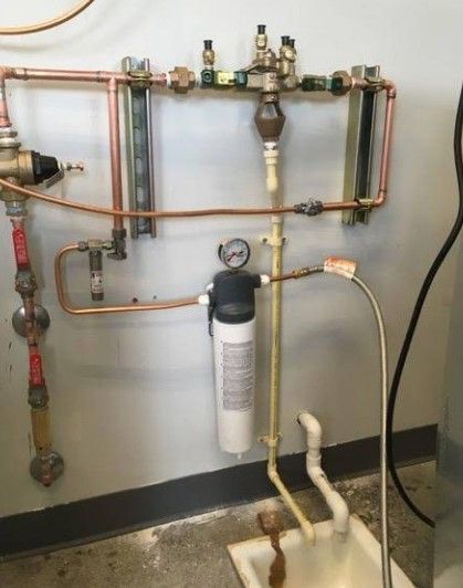 Copper pipes, valves, and filter assembly mounted on a wall in a utility room.