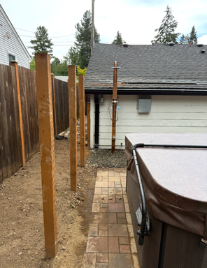 Backyard patio with wooden fence posts and a covered hot tub beside a garage