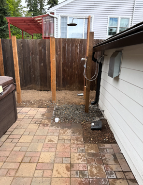 Backyard patio with outdoor shower posts beside a wooden fence and house wall