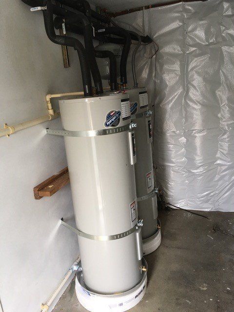 Two tall, gray water heaters in a utility closet. Black pipes connect to the top.