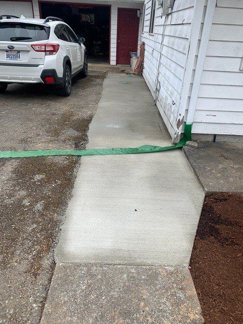 A concrete sidewalk next to a house and driveway, with a car parked near the garage.
