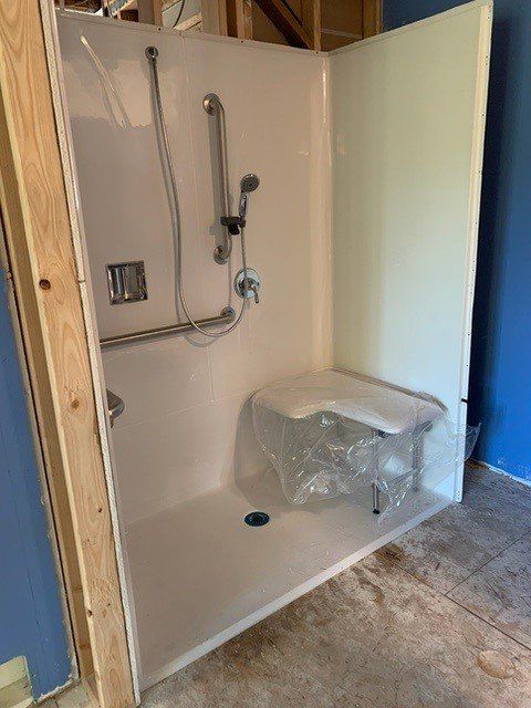White accessible shower with a built-in seat and grab bars. Unfinished construction setting.