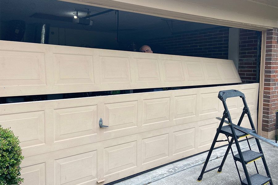Beige garage door partially open; person looking from inside. Black stepladder on the right.