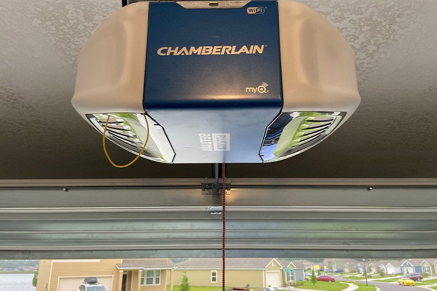 Chamberlain garage door opener unit installed on a ceiling. Blue and white with a red emergency cord hanging down.