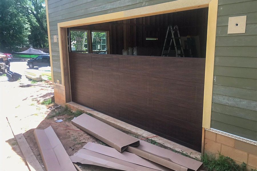 Garage under construction, brown panels installed, beige trim, green siding, outdoor setting.