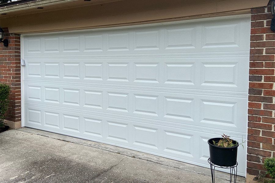 White panel garage door on a brick house; potted plant in front.