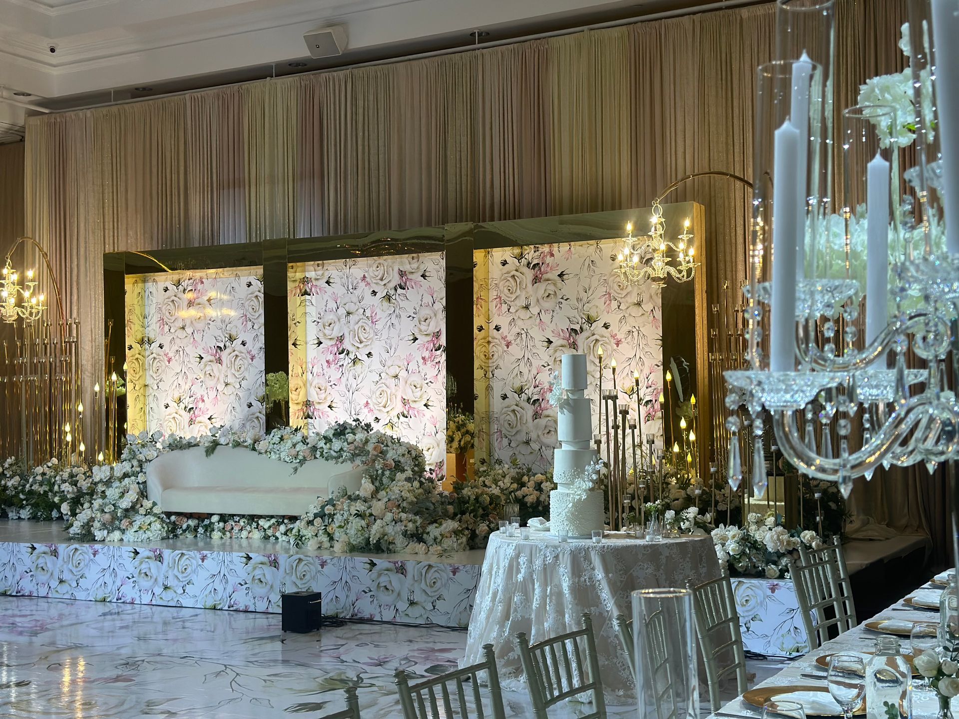 Flowery Indian wedding reception decor on stage and backdrop with a white wedding cake in the foreground