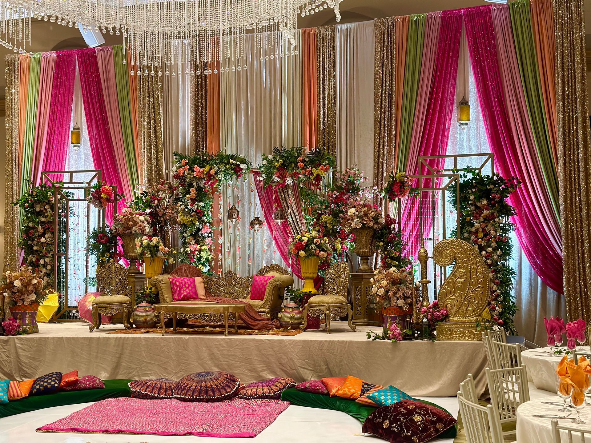 Pink drapes and lanterns hanging on a backdrop behind a reception stage for an Indian wedding covered with flowers