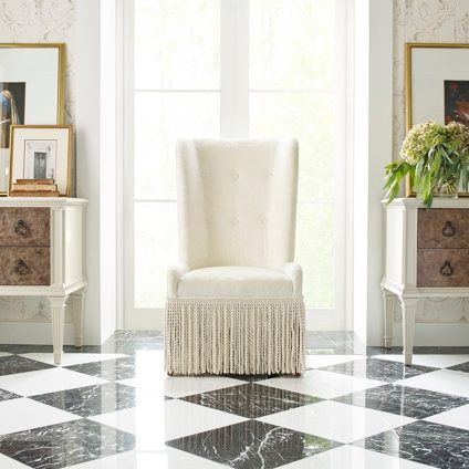 A white chair with fringe is sitting in a room with a checkered floor.