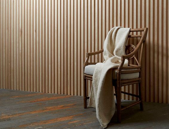 A chair with a blanket on it is sitting in front of a wooden wall.