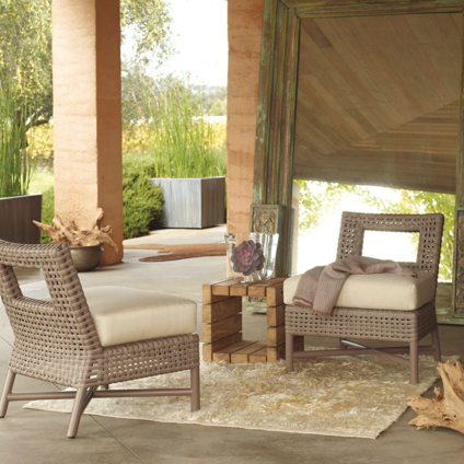 Two wicker chairs are sitting on a rug on a porch