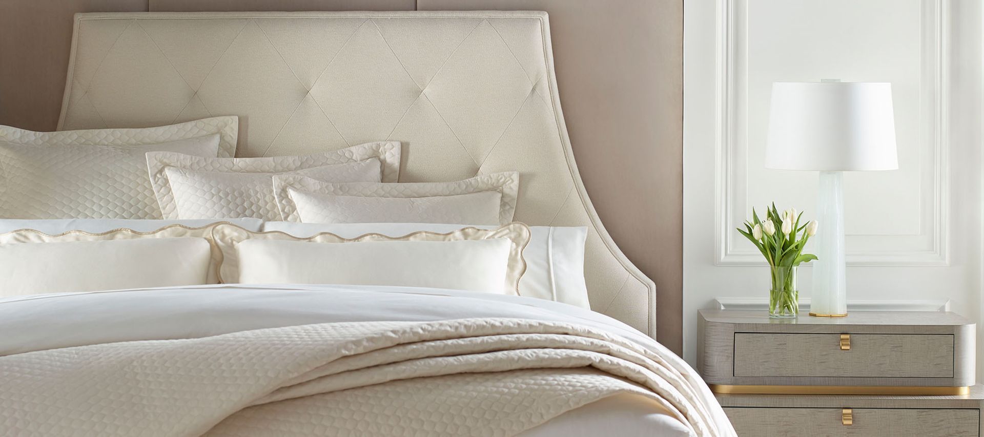 A bedroom with a bed , nightstand , lamp and vase of flowers.