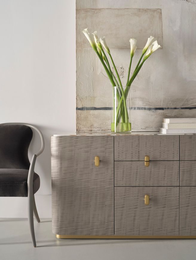 A vase of flowers is sitting on top of a dresser next to a chair.