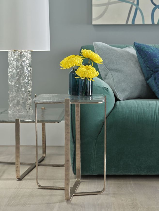 A living room with a green couch and a glass table with yellow flowers on it