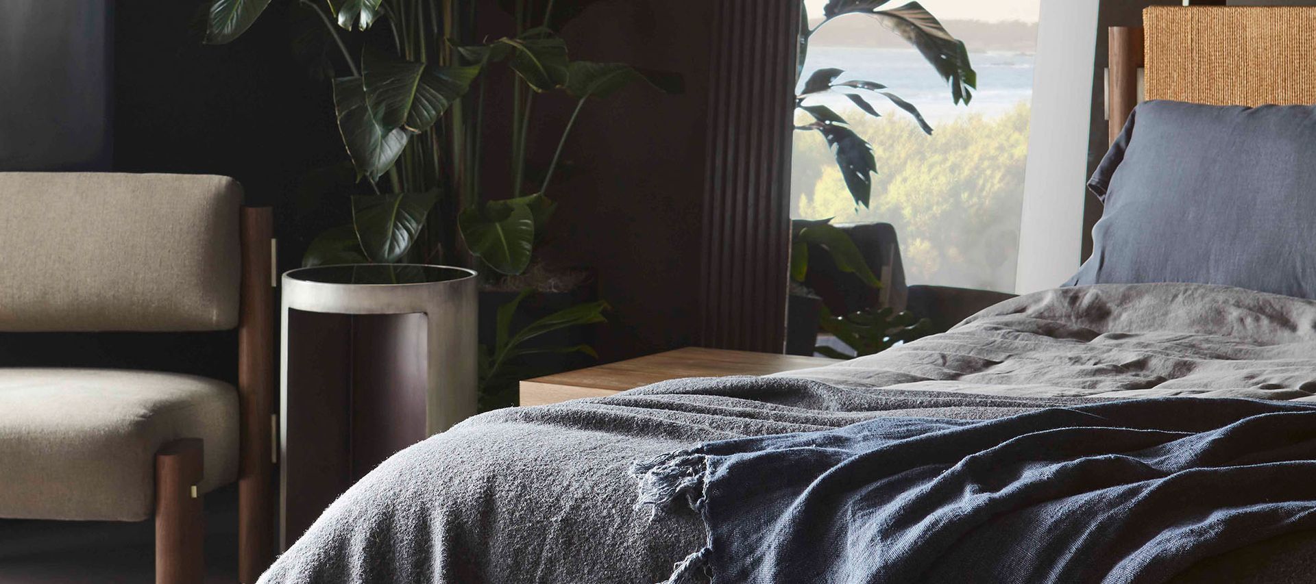 A bedroom with a bed , chair , nightstand and plant.