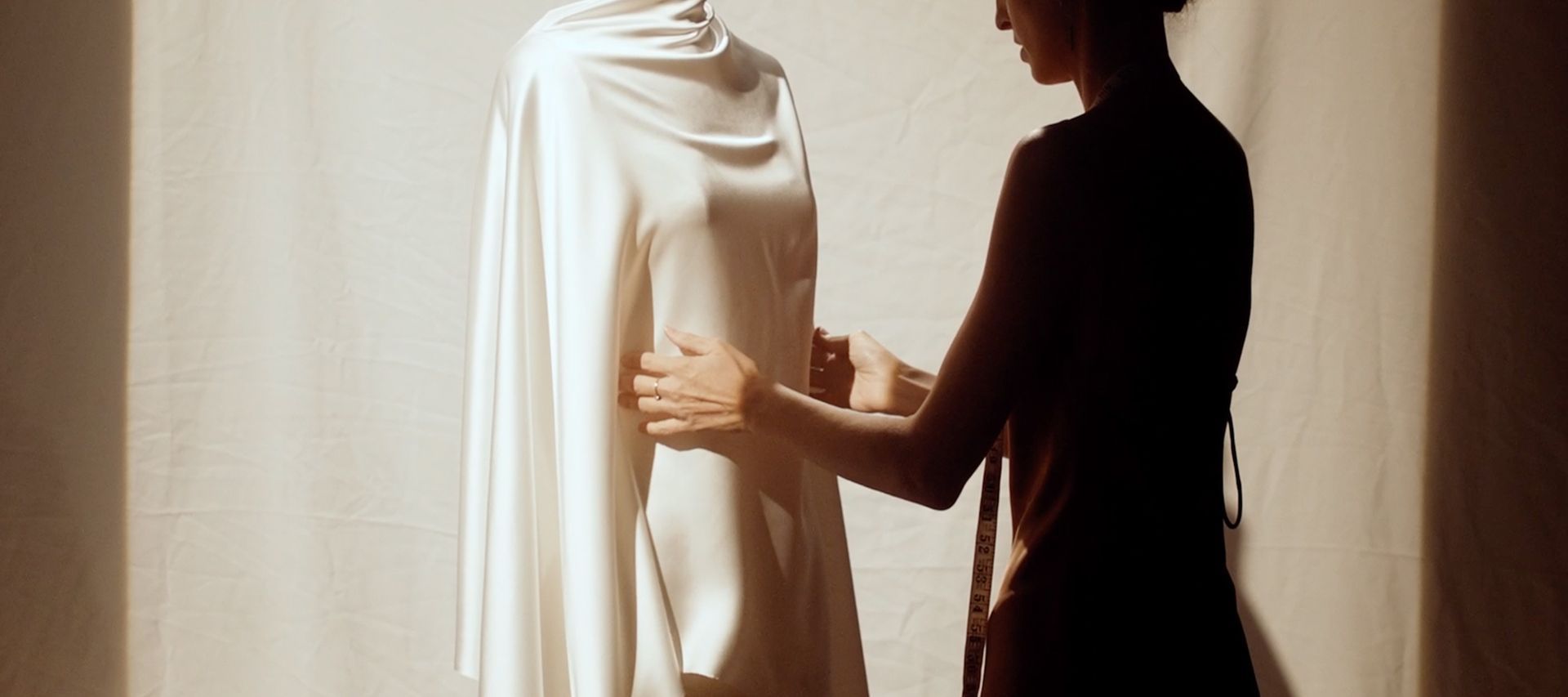 A woman is standing next to a mannequin wearing a white dress.