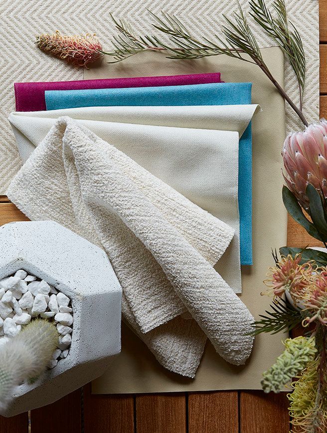 A stack of towels sitting on top of a wooden table next to a vase of flowers.