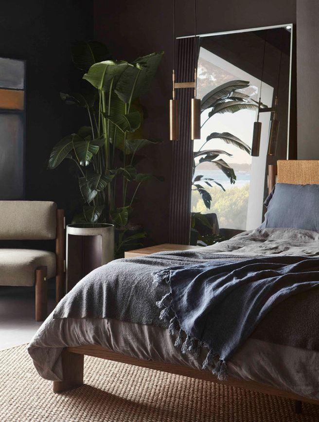 A bedroom with a bed , chair , plant and mirror.