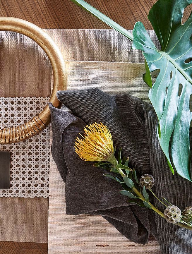 A napkin with a yellow flower on it is sitting on a wooden table next to a plant.