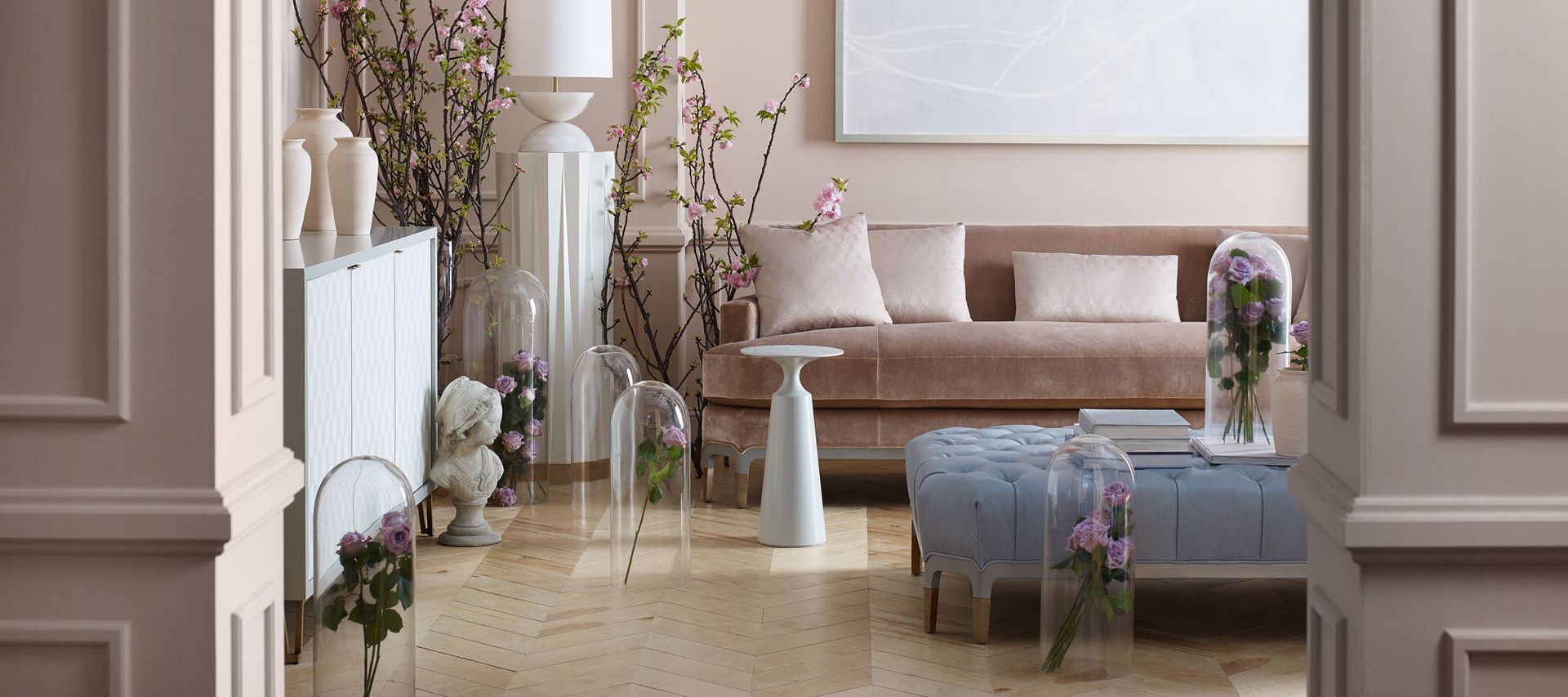 A living room with a couch , ottoman , table and vases of flowers.